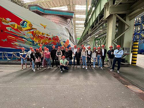 Gruppenbild der Teilnehmer in der Werkshalle der MV-Werften vor dem im Bau befindlichen Schiff "Global-One"