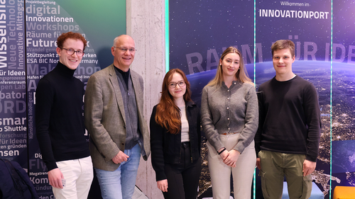Five people are standing side by side and smiling at the camera. In the background, there is a wall with the writing ‘Innovation Port’ and graphic elements on the topic of innovation and space travel.