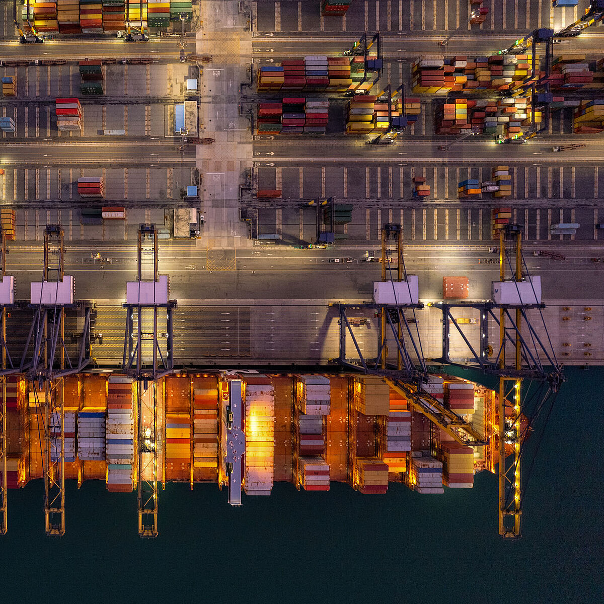 Introduction_Image Studiengang DLM Master Auf einem Seehafengelände werden Container auf ein Schiff umgeschlagen. Draufsicht.