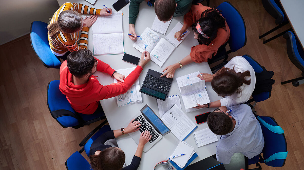 Introduction_Image Studiengang Wirtschaftsrecht Master Studierende sitzen um einen Tisch herum auf dem Unterlagen verstreut sind, Draufsicht
