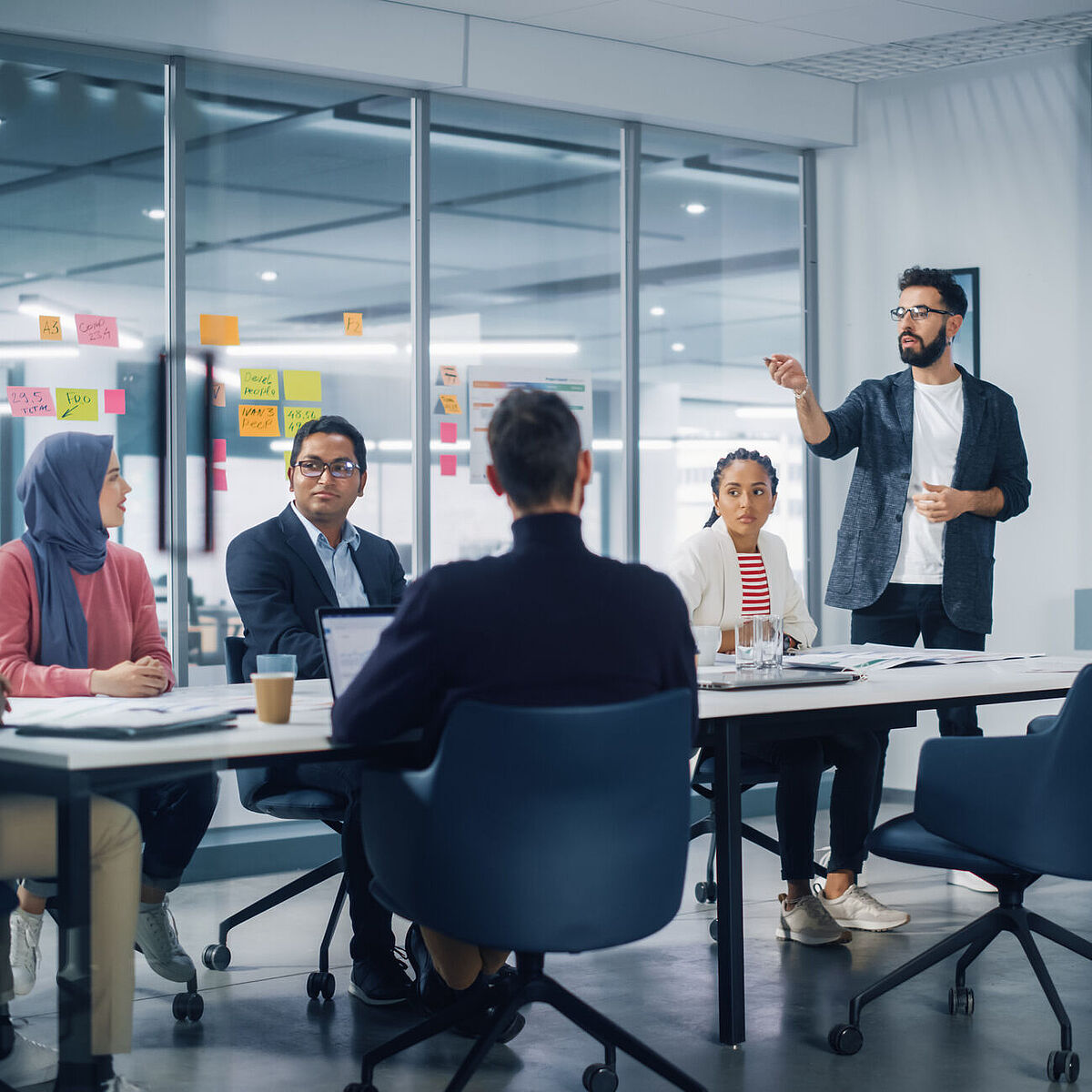 Personen sitzen um einen Konferenztisch während eine Person präsentiert